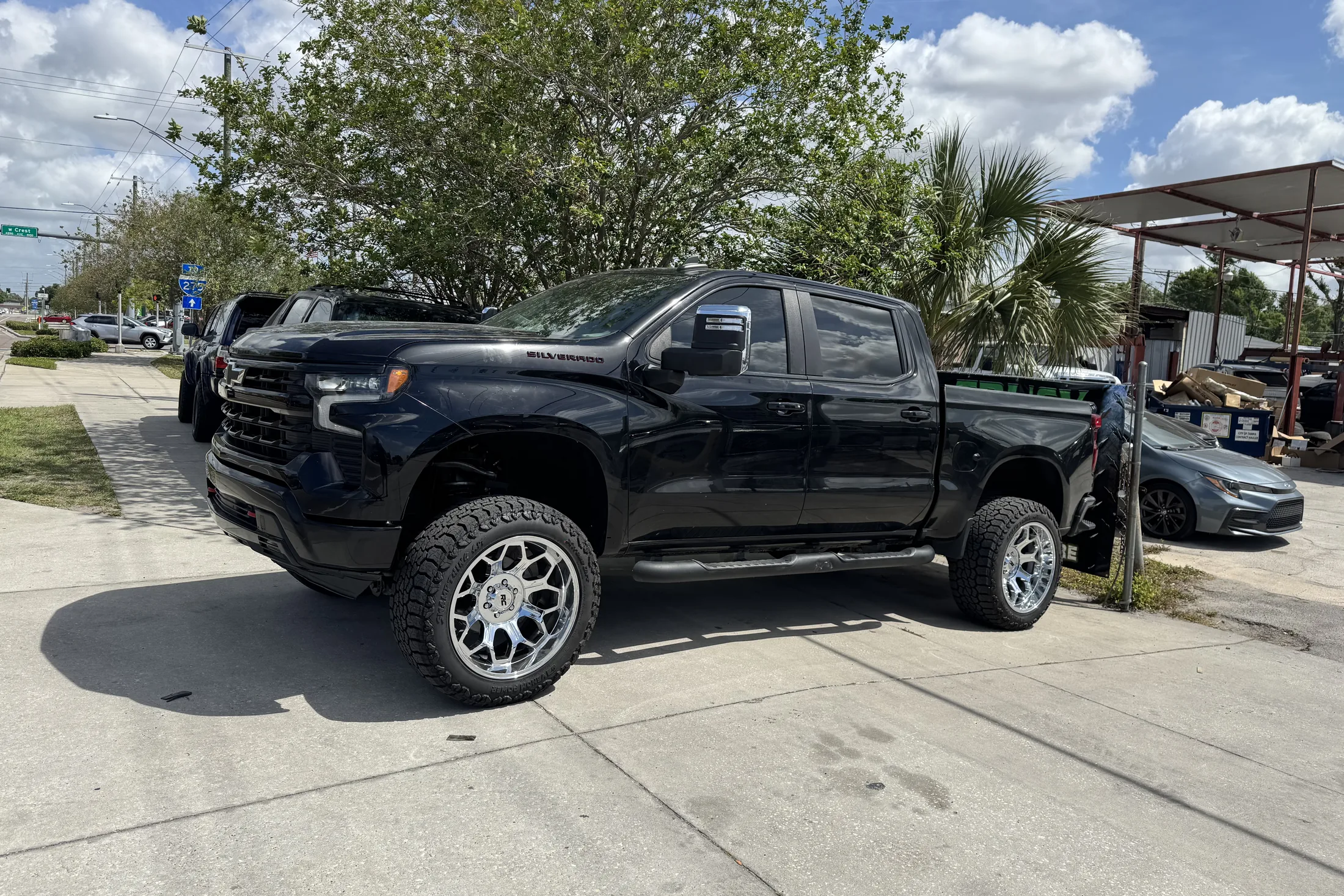 A black lifted Chevy Silverado crew cab on polished wheels outside the shop