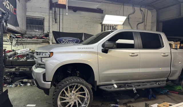A silver Chevy Silverado crew cab up on the lift inside the shop bay