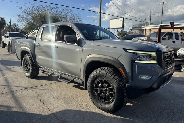 A gray Nissan Frontier on black wheels with all-terrain tires outside the shop