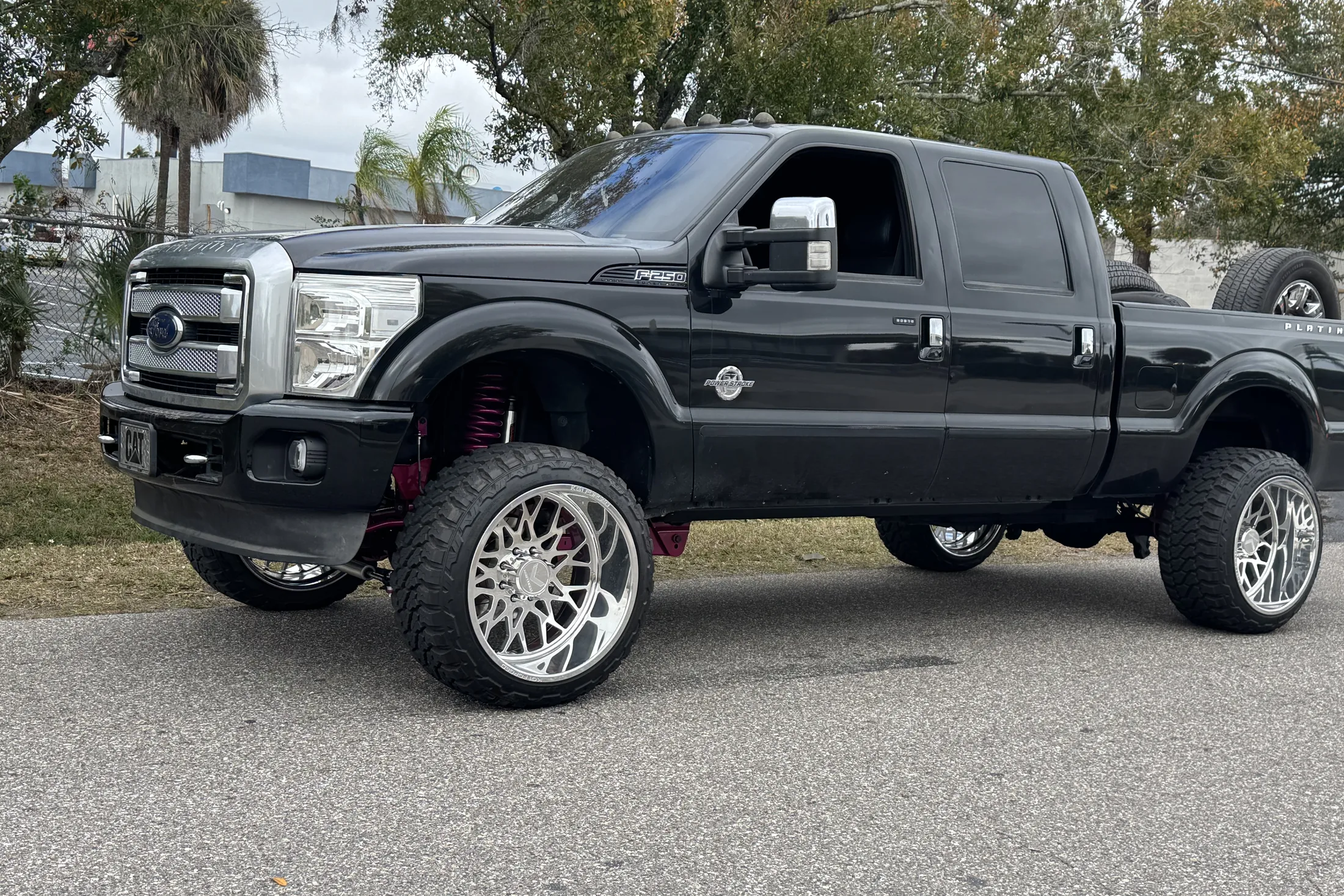 A black Ford F-250 on a lift kit and polished wheels parked on the street outside the shop