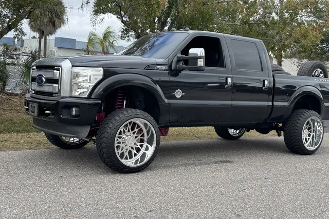 A black Ford F-250 on a lift kit and polished wheels parked on the street outside the shop