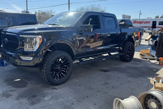 A black Ford F-150 on a lift kit and black wheels parked at the shop