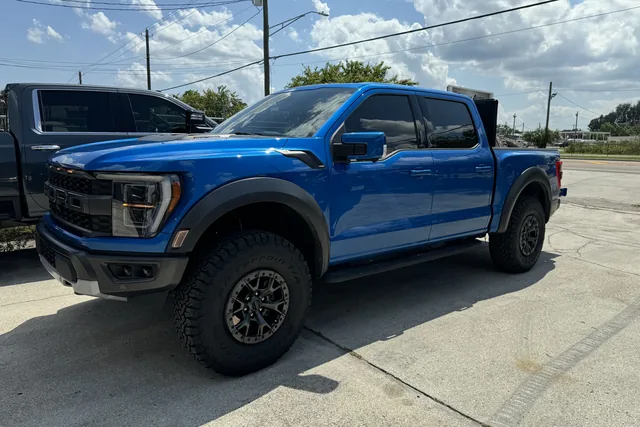 A blue Ford Raptor at stock height on bronze wheels outside the shop