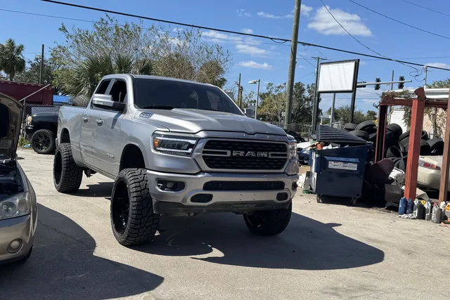 A silver Ram 1500 on a lift kit and black wheels outside the shop