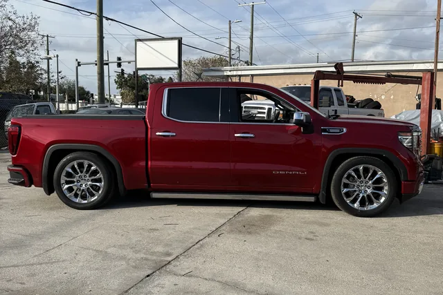 A red GMC Sierra Denali crew cab lowered on polished chrome wheels, parked side on at the shop