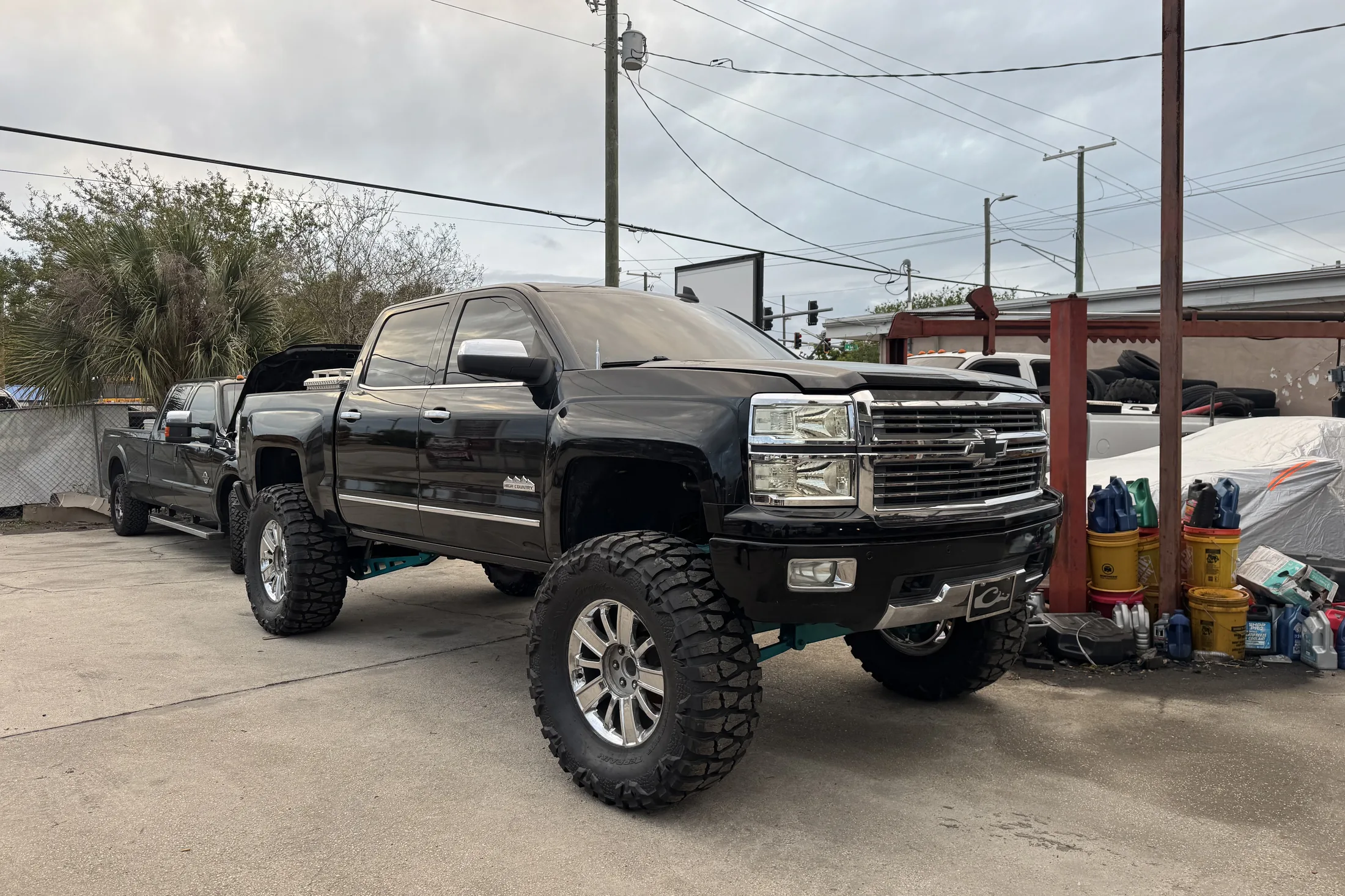 A black lifted Chevy Silverado HD on chrome wheels outside the shop with another truck behind it
