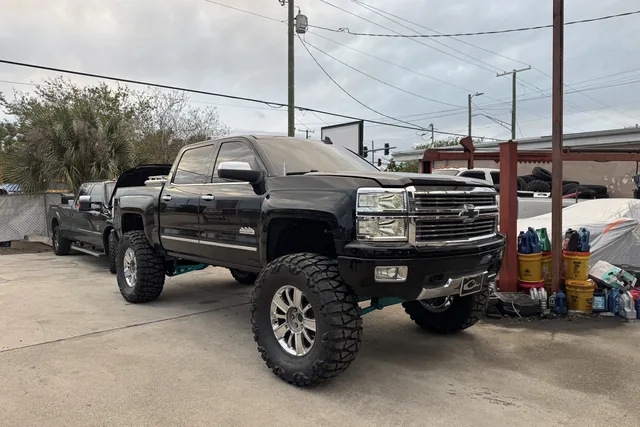 A black lifted Chevy Silverado HD on chrome wheels outside the shop with another truck behind it