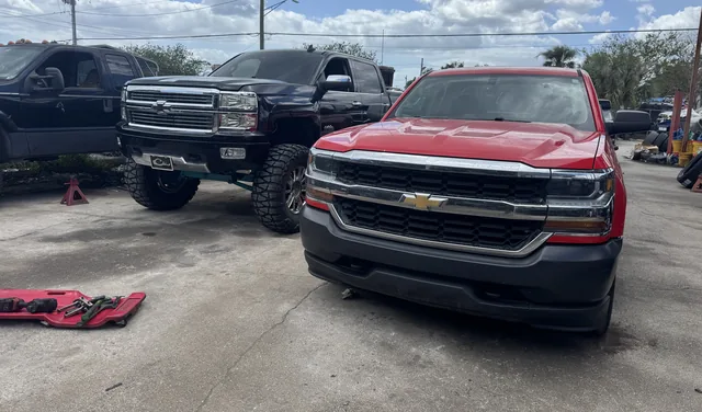 A black lifted Chevy Silverado next to a red Chevy Silverado at stock height outside the shop