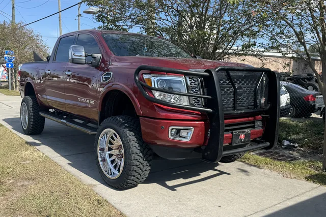 A dark red Nissan Titan XD with a grille guard, lifted on chrome forged wheels