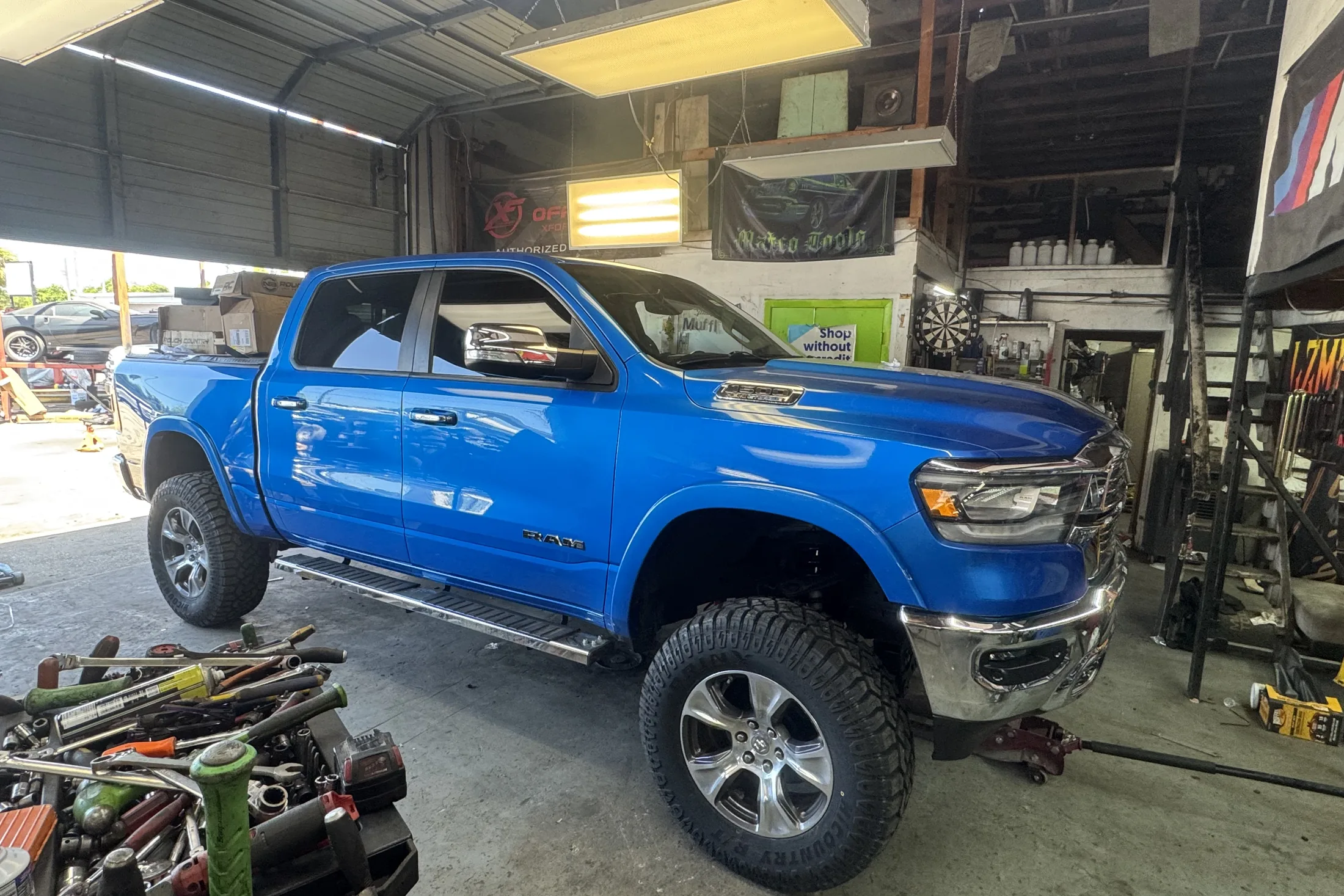 A blue Ram 1500 inside the shop bay beside the lime green bay door