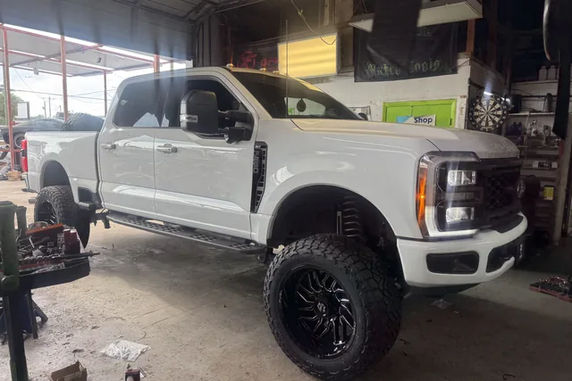 A white Ford Super Duty lifted on black wheels inside the bay beside the lime green door