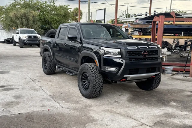 A black Nissan Frontier on a lift kit and black wheels at the shop