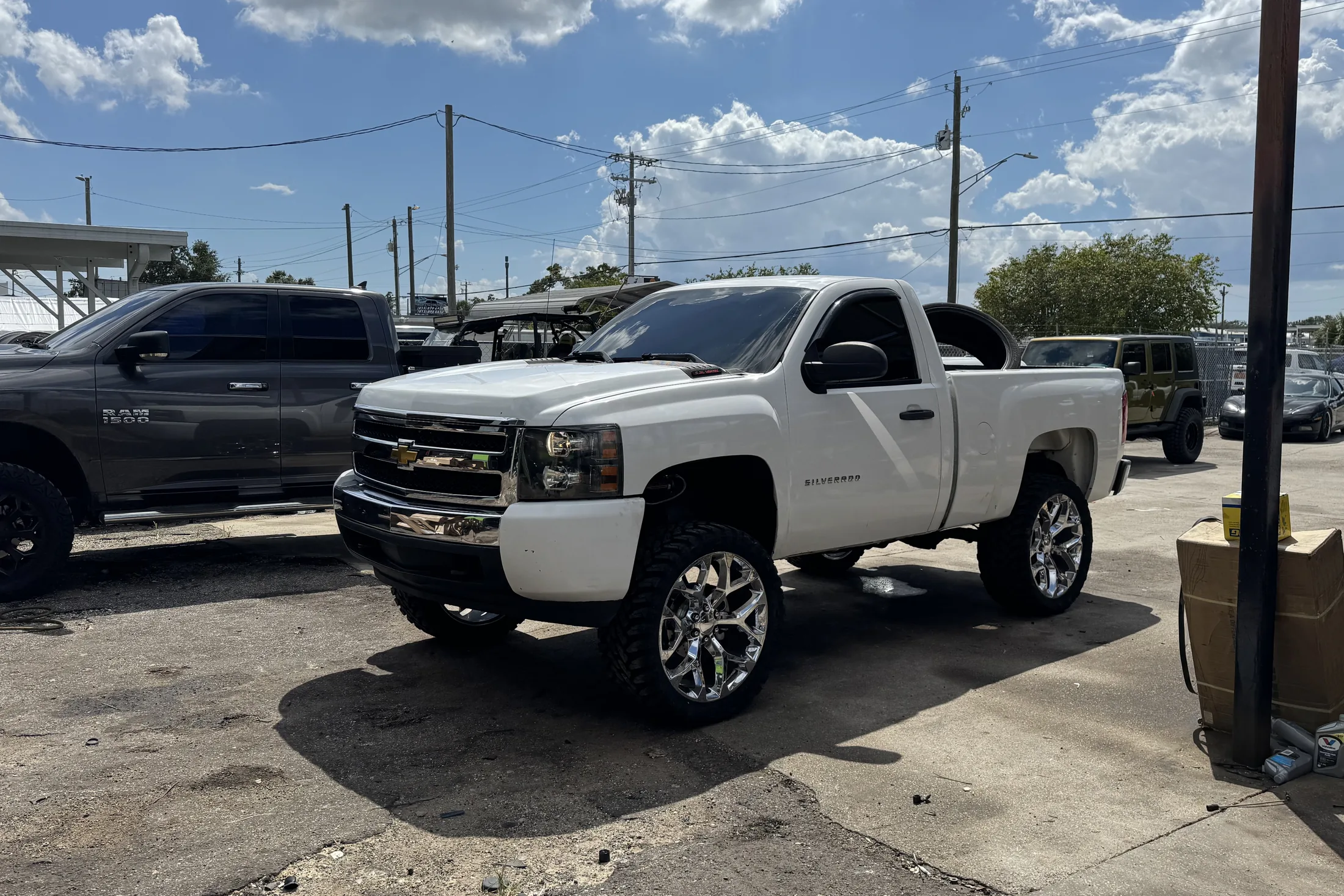 A white Chevy Silverado on a lift kit and polished wheels outside the shop