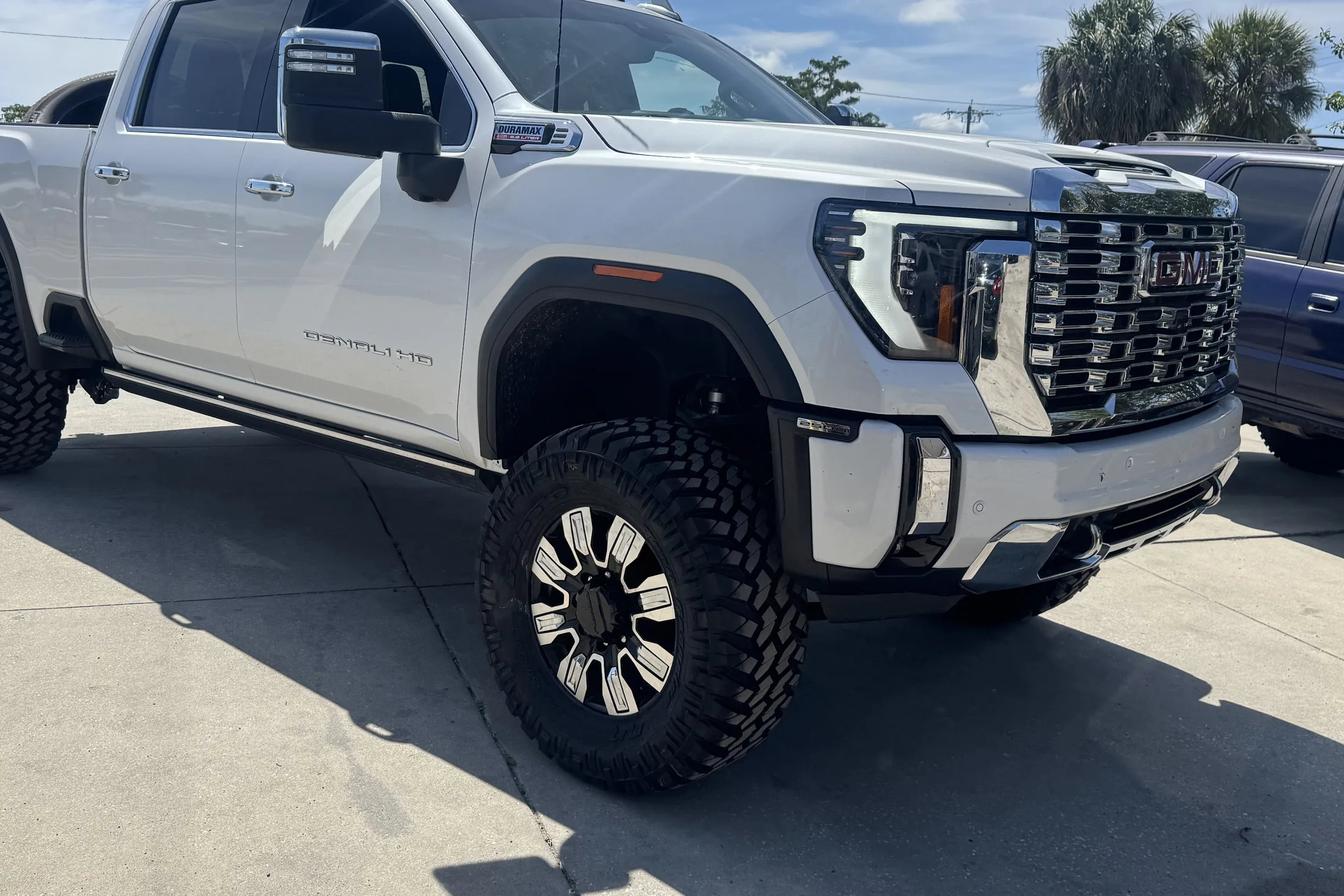 Front three quarter of a white GMC Sierra HD on machined black wheels with off-road tires