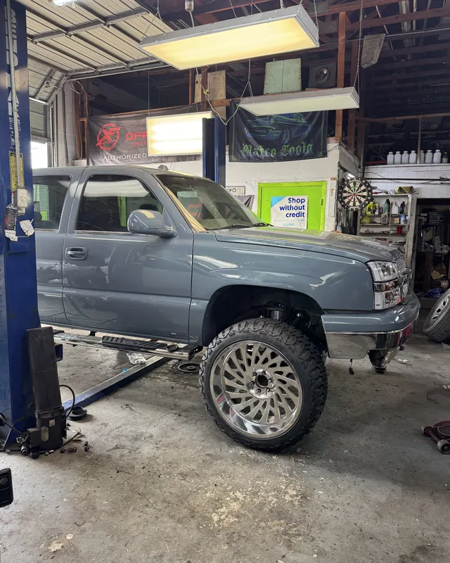 A gray Chevy Silverado on polished wheels raised on the two-post lift inside the shop