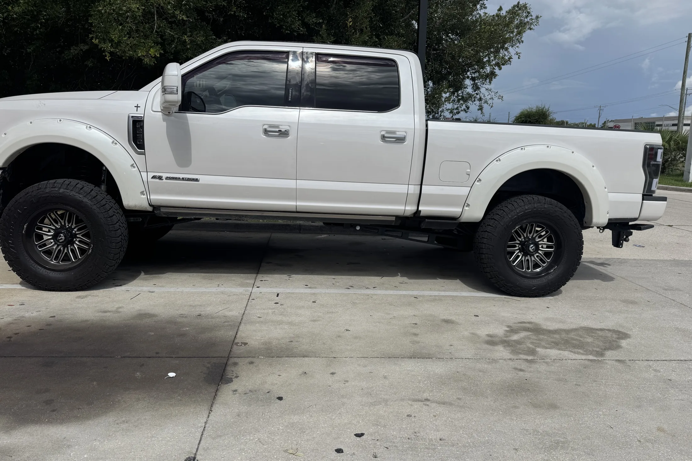 A white Ford Super Duty crew cab on black wheels seen from the side outside the shop