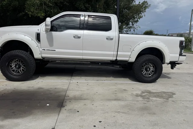 A white Ford Super Duty crew cab on black wheels seen from the side outside the shop