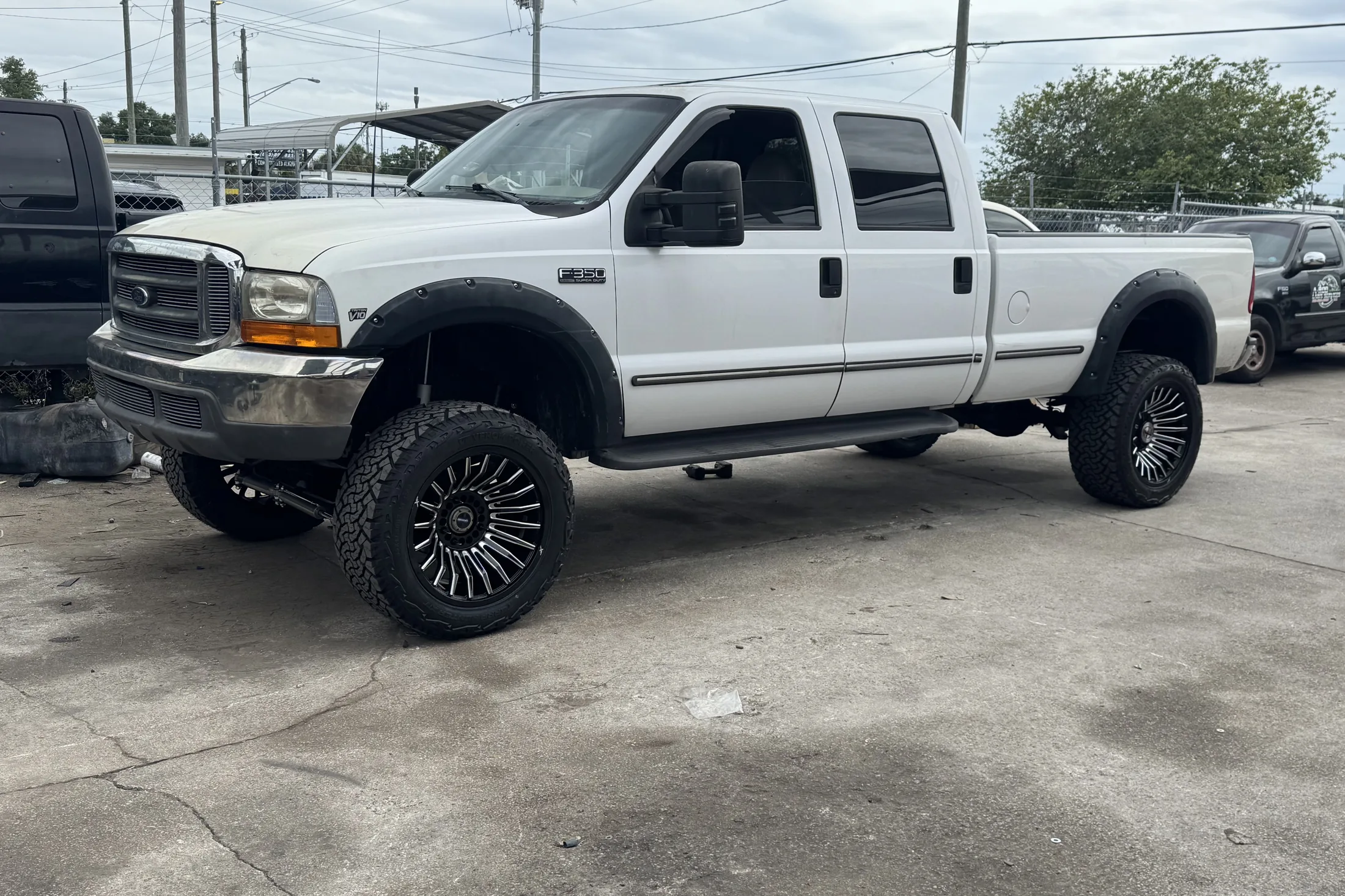 A white Ford Super Duty pickup on black wheels outside the shop