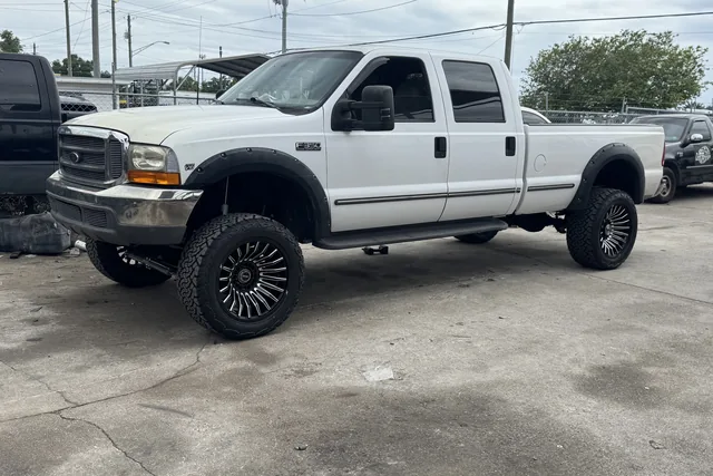 A white Ford Super Duty pickup on black wheels outside the shop