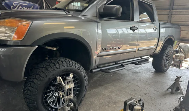 A gray Nissan Titan on the lift inside the shop bay with off-road tires