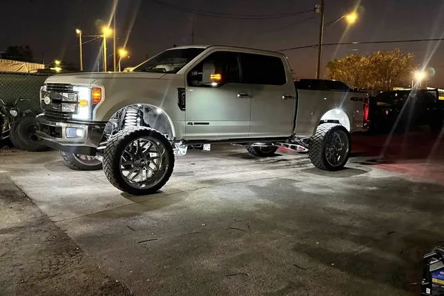 A tan Ford Super Duty at night with rock lights lit under the truck, front three quarter